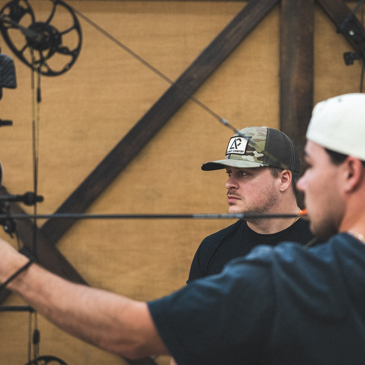 Two men with archery equipment in a workshop setting
