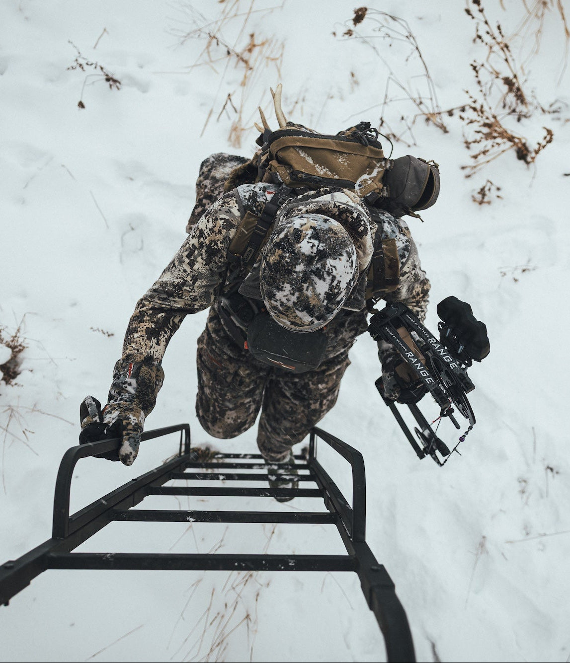 Person in camouflage gear climbing a ladder in a snowy landscape