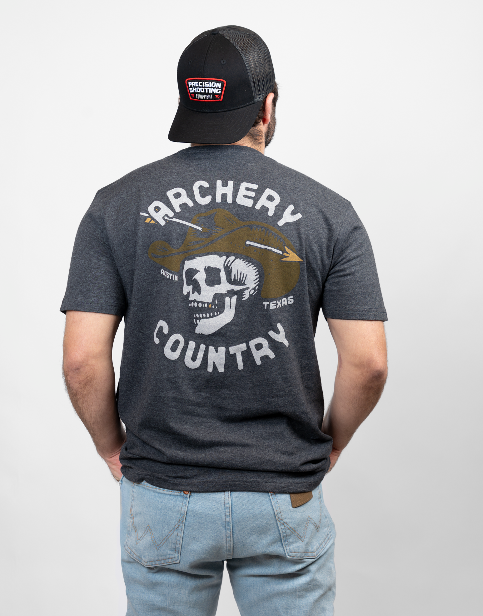 Rear view of man wearing charcoal tee with graphic of  a skull wearing a cowboy hat with an arrow through it with text "ARCHERY COUNTRY AUSTIN TEXAS"