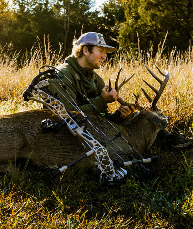 Man with a bow and arrow next to a deer in a grassy field