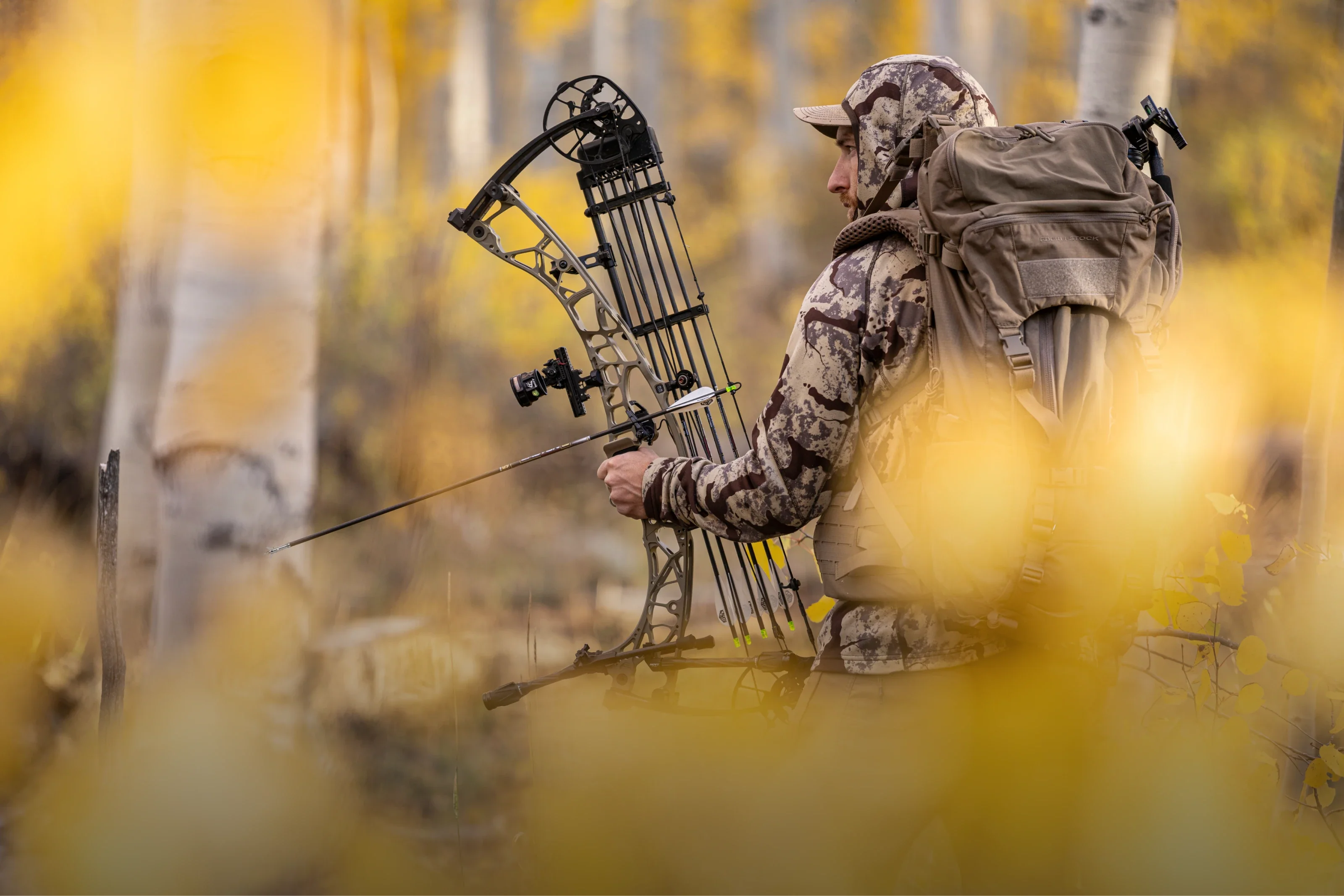 Hunter in camouflage gear with a bow in a forest setting