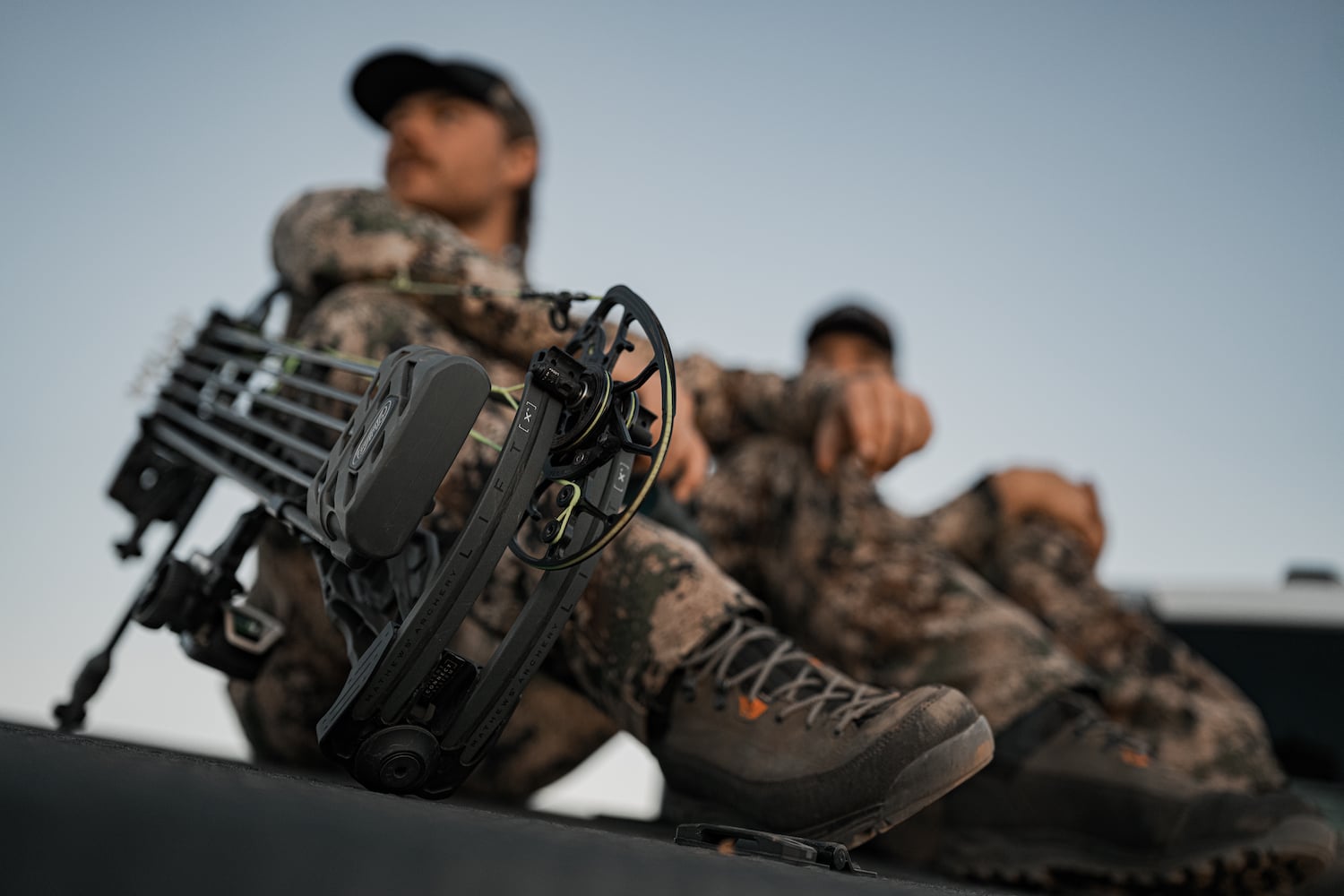 Person in camouflage gear with a crossbow, sitting on a vehicle.