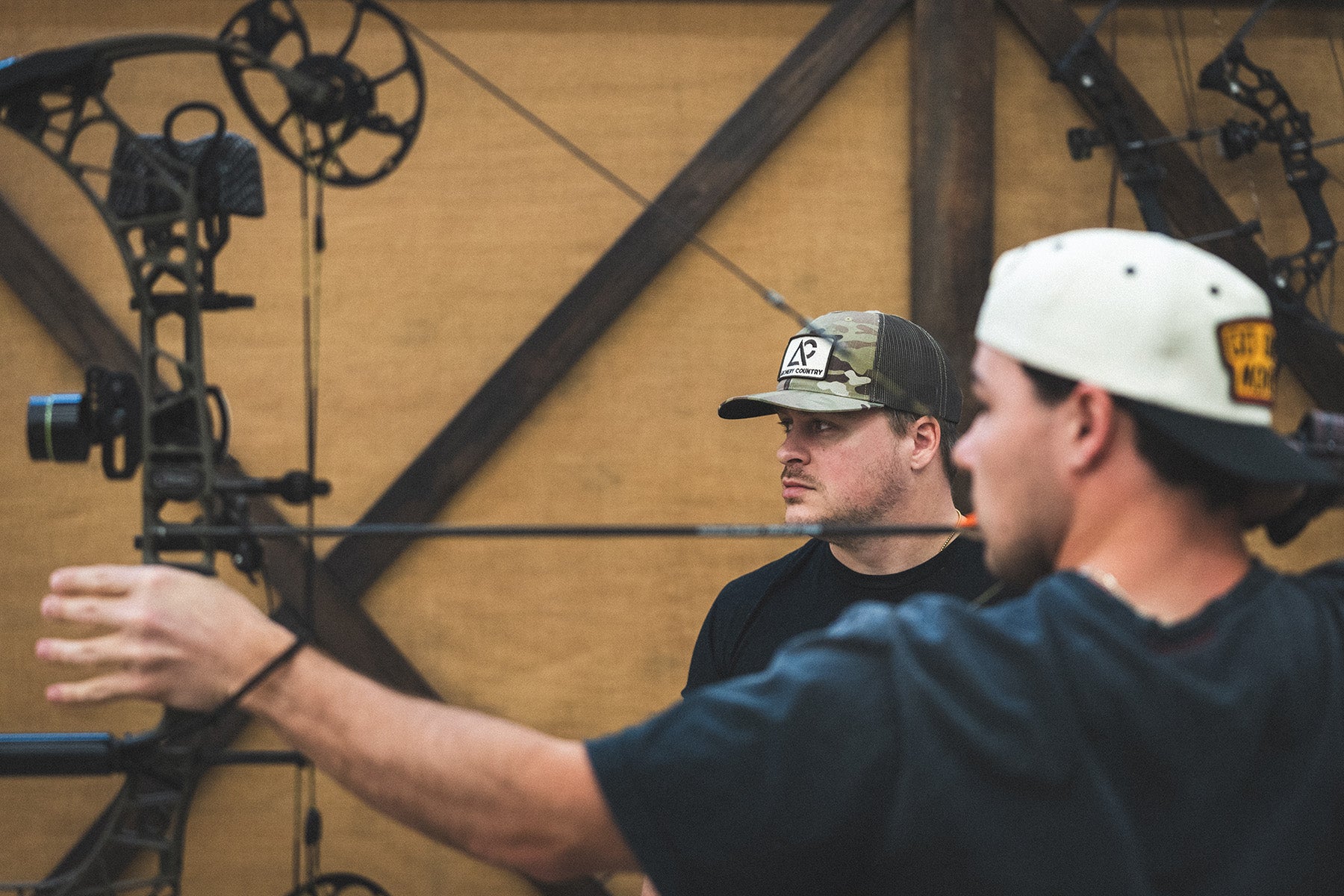 Two men with archery equipment in a workshop setting
