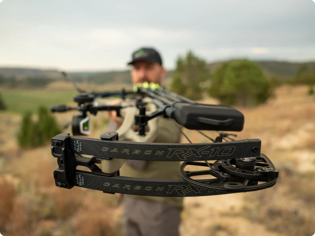 Man holding a crossbow with 'Carbon RX-10' branding in an outdoor setting.